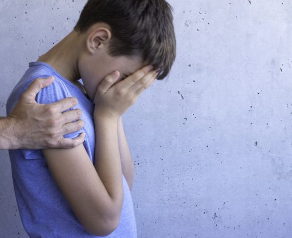 Foto colorida de criança cobrindo o rosto e sendo segurado por adulto. Imagem ilustrativa - Metrópoles