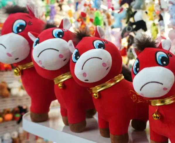 Quatro cavalos de pelúcia com expressão triste. Eles são vermelhos e têm um colar dourado com um sino.