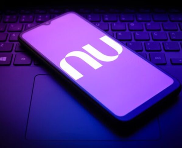 Imagem de telefone celular, em cima de um teclado de notebook, exibindo a logomarca do Nubank
