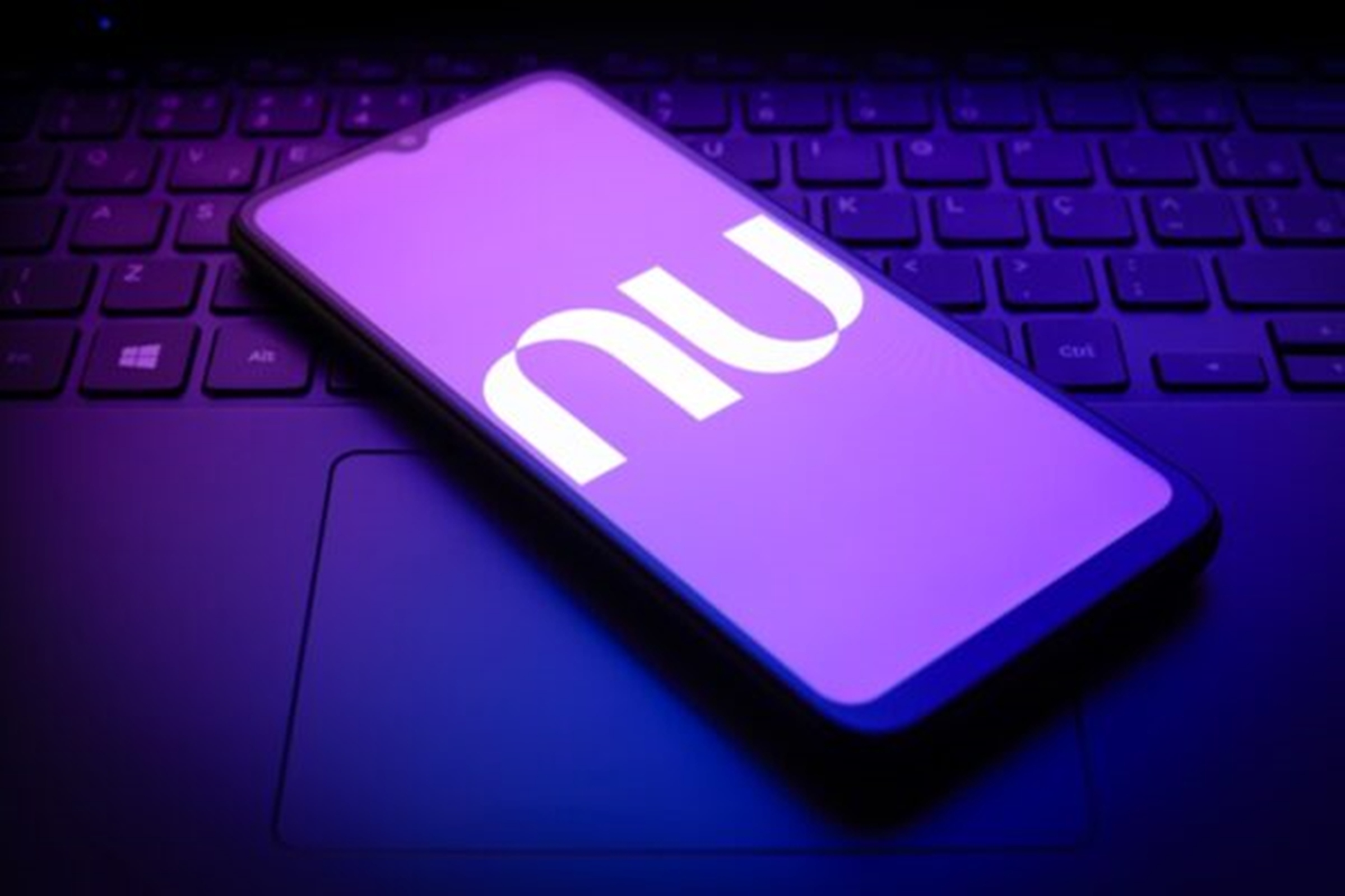 Imagem de telefone celular, em cima de um teclado de notebook, exibindo a logomarca do Nubank